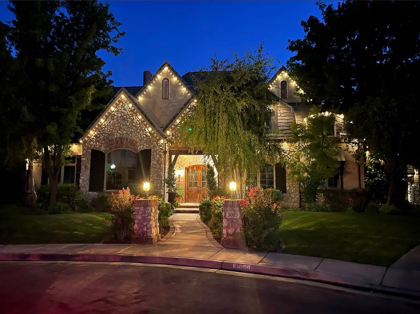 Warm-white roofline lighting on a stone-front home at dusk